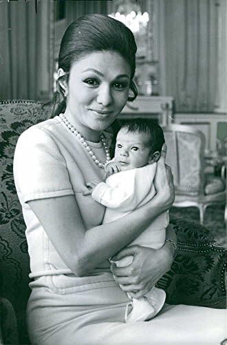 Vintage fotografija Farah Pahlavi nosi svog sina i gleda u kameru.